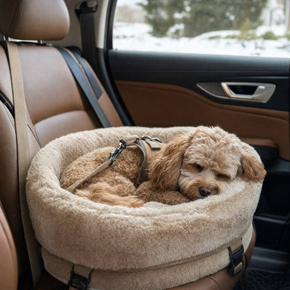 Small dog resting in a cream faux-fur round car bed, harness tether clipped, snow outside