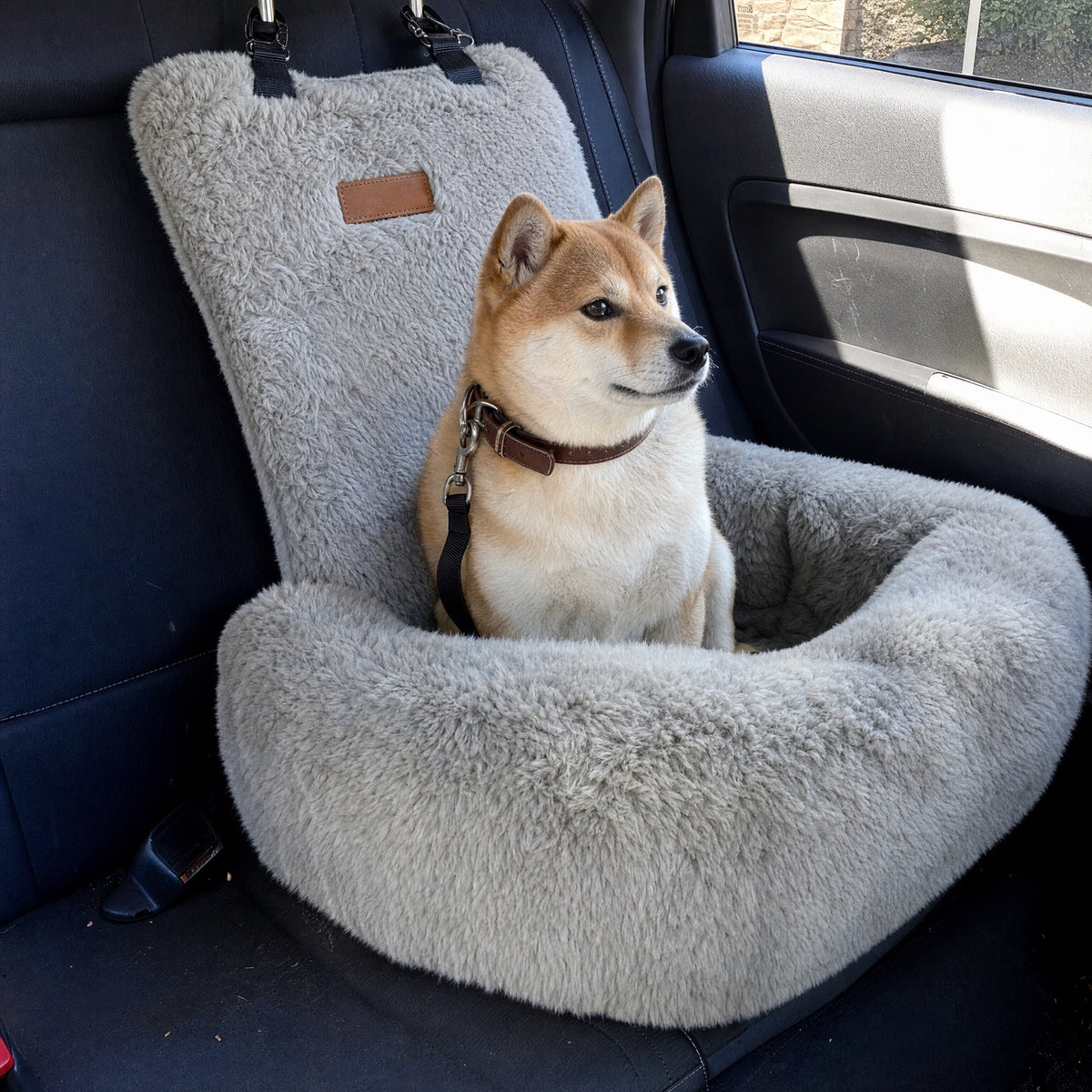 A Shiba Inu sits in a grey Nordpaw lounger car bed on a car back seat, seen from the open rear door